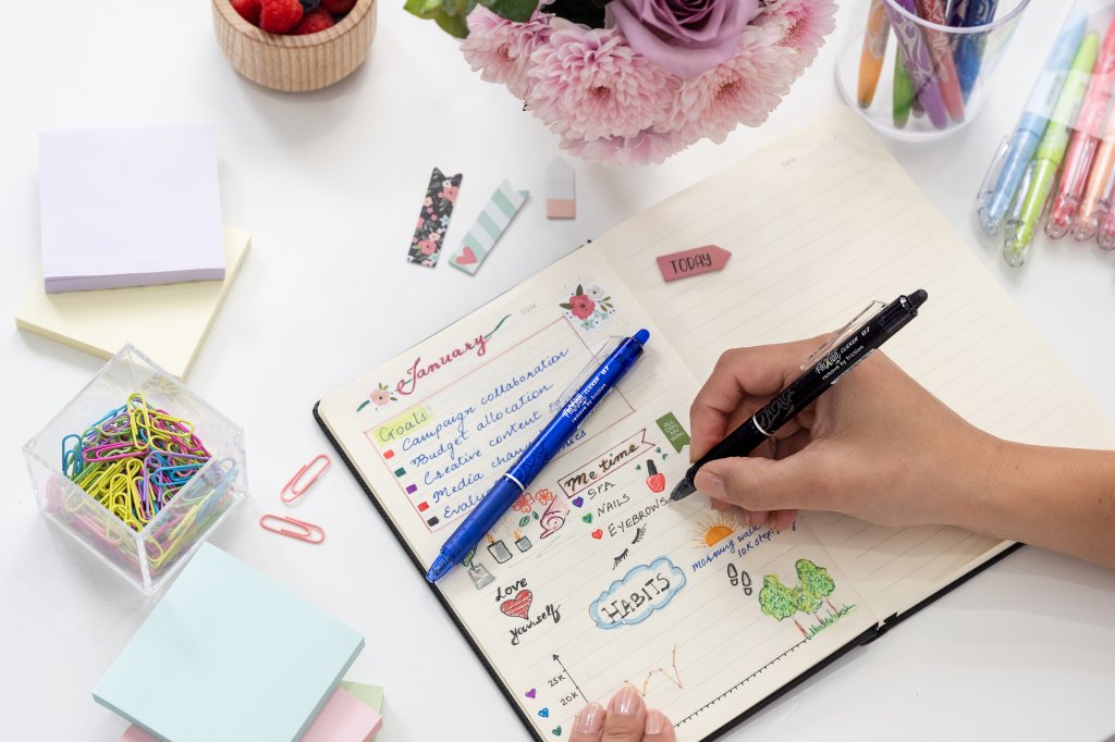 Hand using a FriXion Clicker Erasable Gel Pen to jot down goals and plans in a bullet journal, showcasing the pen's smooth ink and precision.