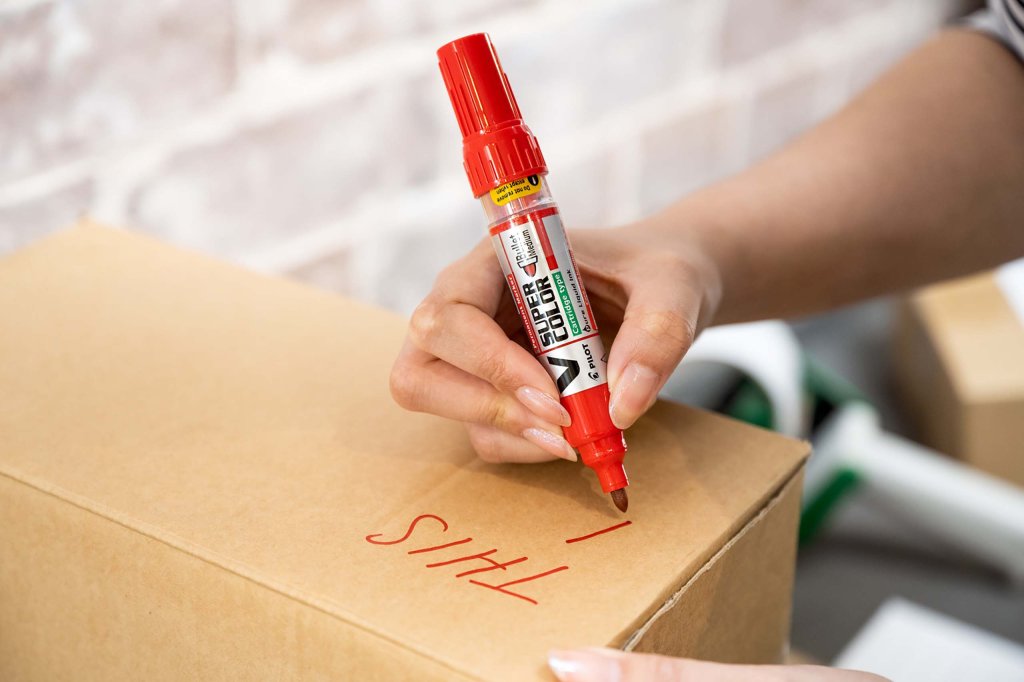 V Super Color Permanent Marker in red by PILOT Pen being used in a warehouse to mark cardboard boxes.