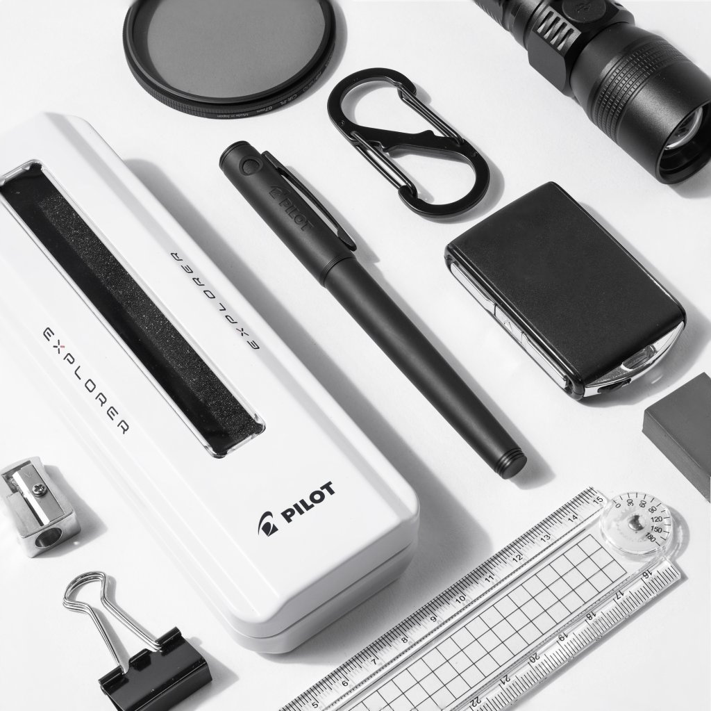 Pilot Explorer pen in Matte Black, in a flat lay, next to items as part of an everyday carry kit, including the Explorer gift box, a carabiner, car key, flashlight and ruler.